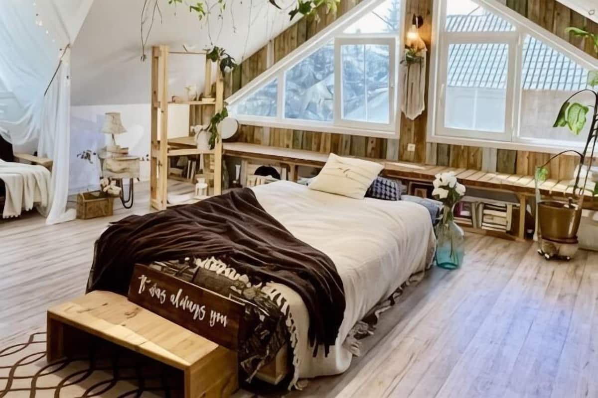 A cozy bedroom with a bed, bedside table, and a window with a view.