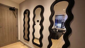 Un pasillo con tres espejos ondulados en la pared, una puerta de madera y, al fondo, un área de estar con un sofá y una mesa de centro.