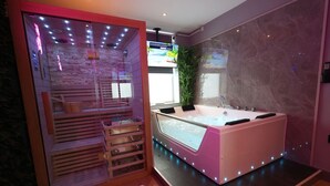 Un spa moderno con una bañera grande, un baño de vapor con paredes de vidrio y un banco de madera.