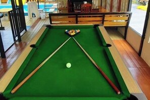A pool table with a cue stick and balls, a wooden bench, and a view of a pool table in the background. - Win Win Villa (Sattahip)