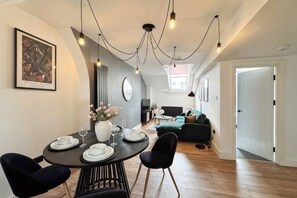 A modern dining area with a round table, black chairs, and a vase of flowers. There is a sofa and a door in the background. - City Retreat on Queen Street (Newcastle)