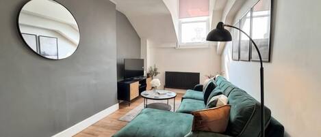 En moderne stue med en grøn sofa, et rundt spejl og et fladskærms-tv.