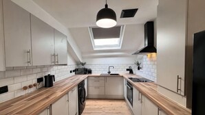 A modern kitchen with white cabinets, wooden countertops, a skylight, and a black pendant light.