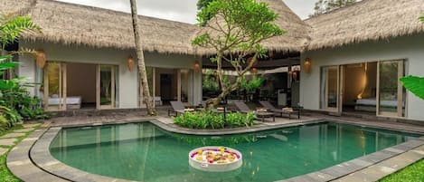 Un área de piscina con un jacuzzi circular, estructuras de techo de paja y un césped bien cuidado.