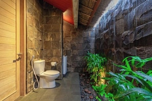 Un baño con pared de piedra, inodoro, ducha y una pequeña zona con plantas.