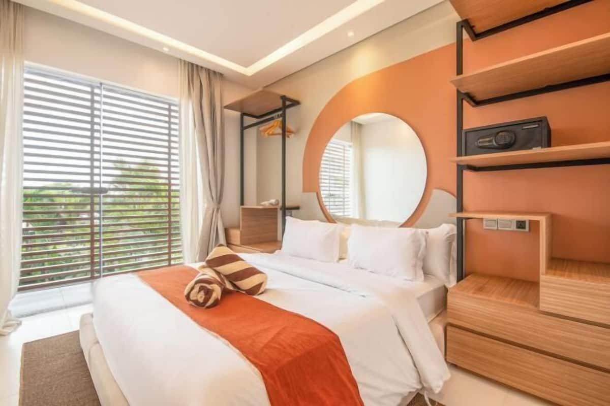 A modern hotel room with a large bed, a round mirror, built-in shelves, and a view through the window.