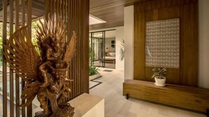 A modern interior with a wooden sculpture, a patterned wall, and a bench with a potted plant. - Swastamita (Bali)