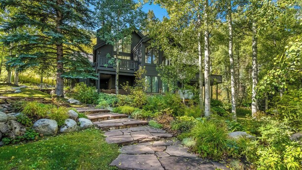 A rustic cabin surrounded by dense forest, with a stone pathway leading to the entrance. - Evergreen Escape - Home for 10 (Vail)