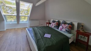 Une chambre avec un puits de lumière, un lit agrémenté d’oreillers à motifs floraux, une table de chevet avec une lampe et un radiateur.