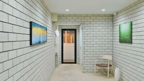 A corridor with white brick walls, two framed artworks, a door, and a chair. - Fandina Tokyo (Tokyo)