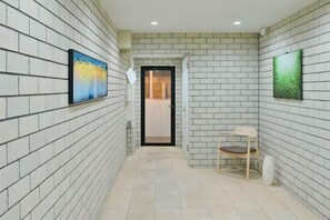 A corridor with white brick walls, two framed artworks, a door, and a chair. - Fandina Tokyo (Tokyo)