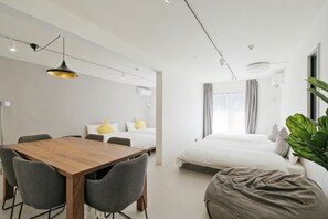 A modern hotel room with a wooden dining table, grey chairs, a large bed, and a bedside plant. - Fandina Tokyo (Tokyo)
