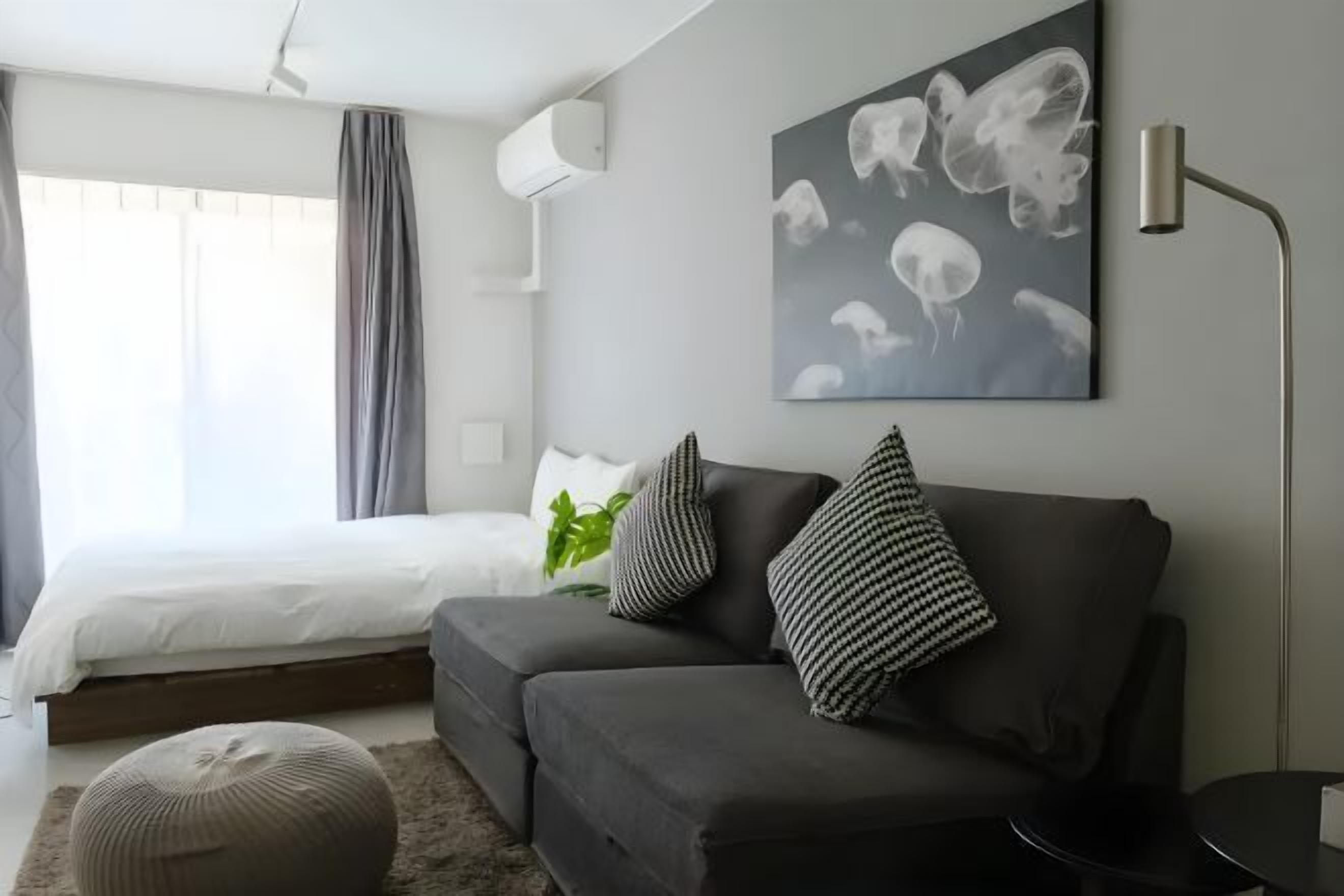 A modern bedroom with a bed, grey sofa, and a wall-mounted artwork.