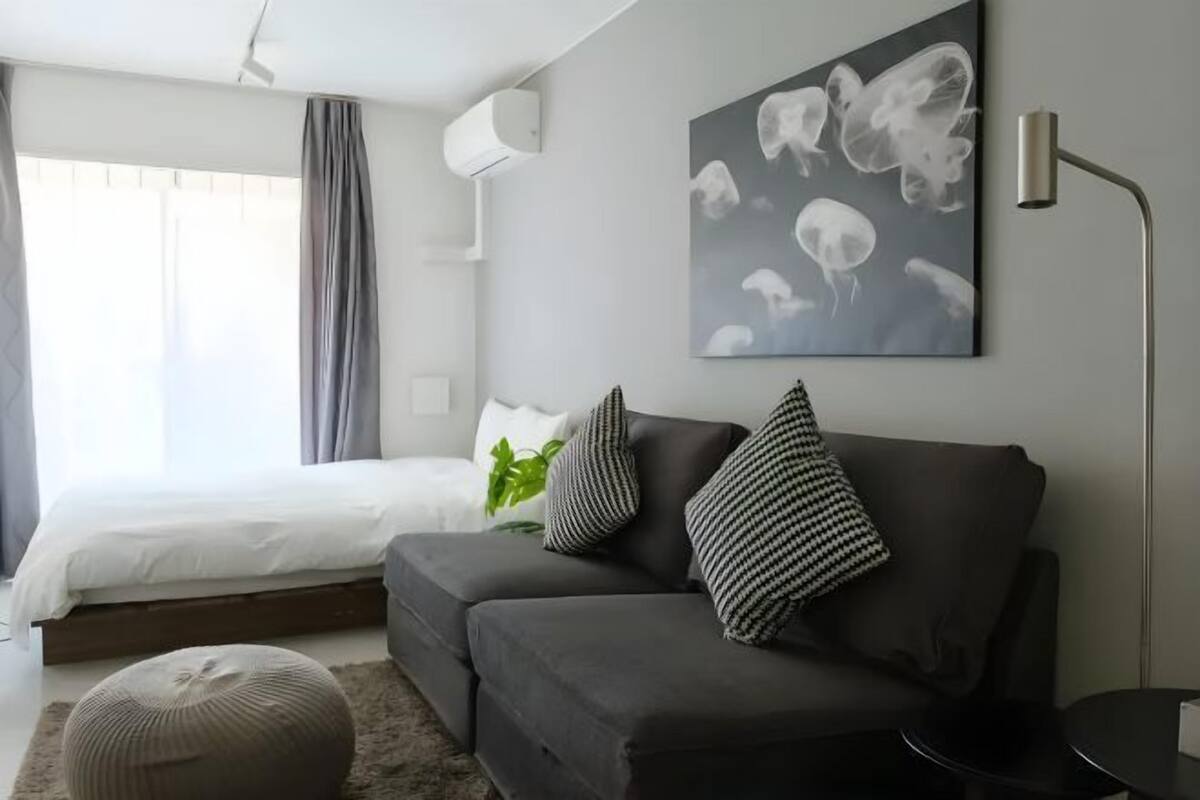 A modern bedroom with a bed, grey sofa, and a wall-mounted artwork.