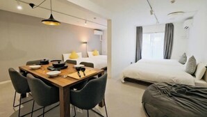A modern hotel room with a wooden dining table, gray chairs, a bed with white bedding, and a gray bean bag. - Fandina Tokyo (Tokyo)