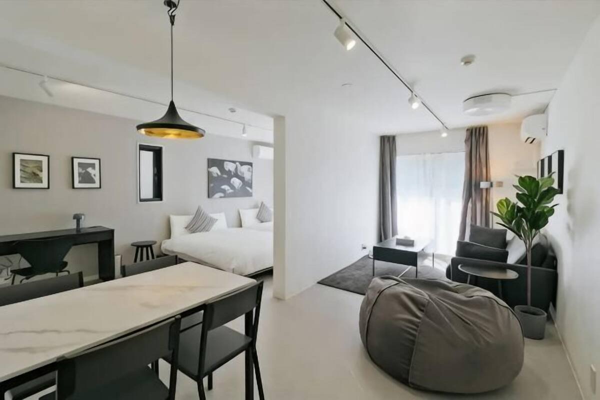 A modern hotel room with a dining area, a bed with pillows, a large bean bag, a potted plant, and a view of the outside.
