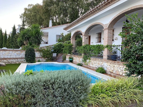 A house with a swimming pool, surrounded by greenery and stone walls.