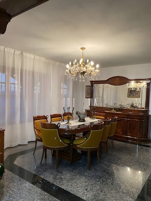 A dining room with a chandelier, wooden dining table, yellow chairs, and a marble floor.