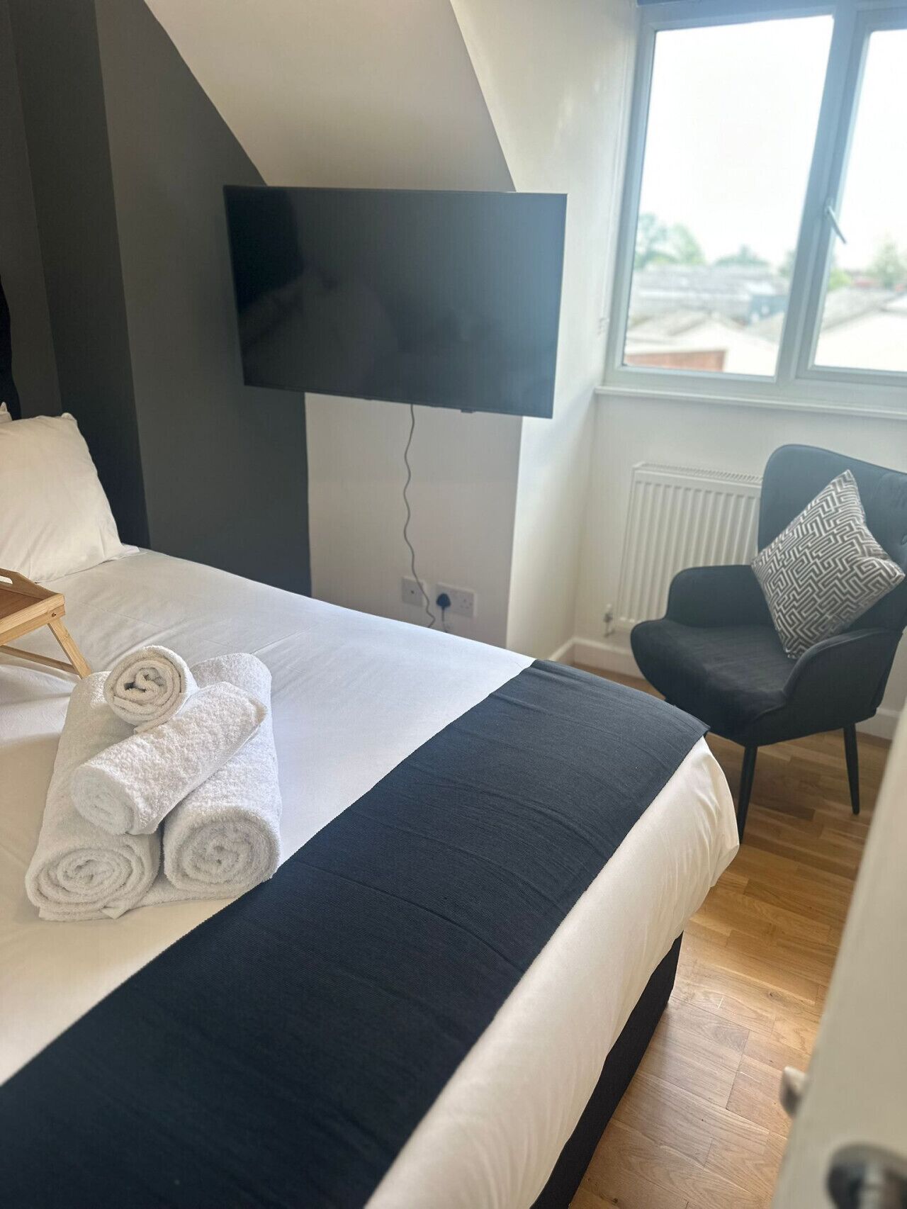 A hotel room with a bed, a chair, a TV mounted on the wall, and a window with a view of the outside.