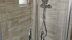 Una cabina doccia in vetro con soffione a mano e rubinetto a parete.