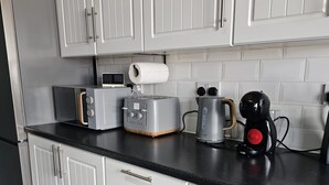 Una cucina moderna con mobili bianchi, un piano di lavoro nero e vari elettrodomestici, tra cui un tostapane, un bollitore e una macchina da caffè.