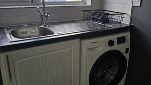 Una cucina compatta con lavatrice e asciugatrice integrate, una finestra vista su un edificio e una rastrelliera metallica per stendere i panni.