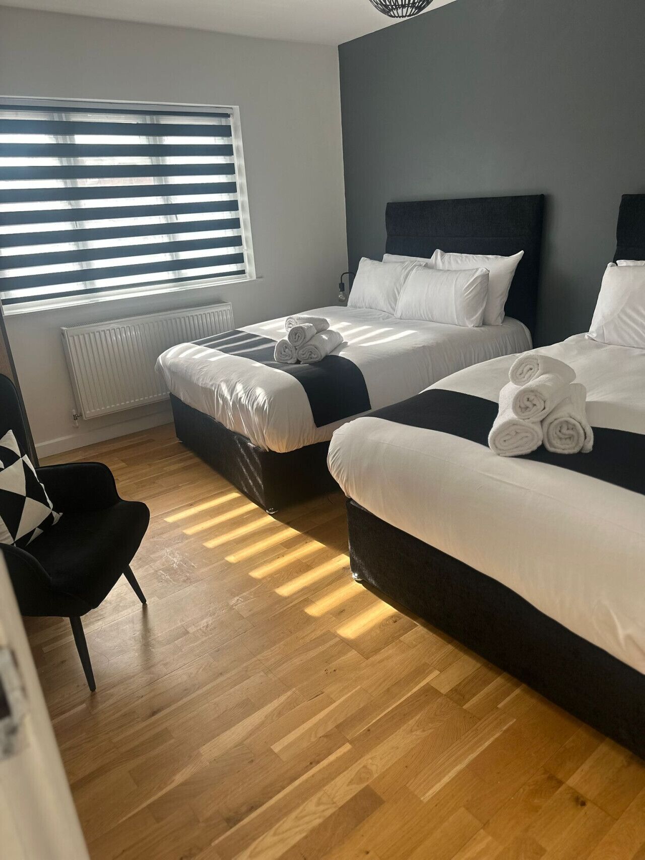 A hotel room with two beds, a radiator, a chair, and a window with blinds.