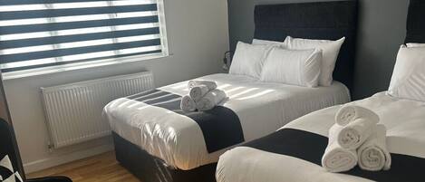 A hotel room with two beds, a radiator, a chair, and a window with blinds.