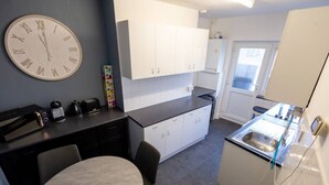 Een kleine keuken met witte kastjes, een ronde tafel en een grote klok aan de muur.