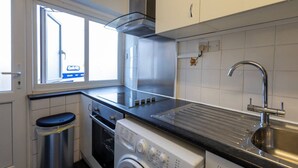 Een kleine keuken met een roestvrijstalen afzuigkap, een inbouwoven, een wasmachine en een spoelbak.