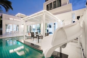 A modern hotel with a pool, outdoor seating, and a slide.