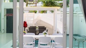 Ein Hotelzimmer mit Balkon, einem Essbereich mit weißen Stühlen und einem Tisch sowie Blick auf die umliegenden Gebäude und Grünflächen.