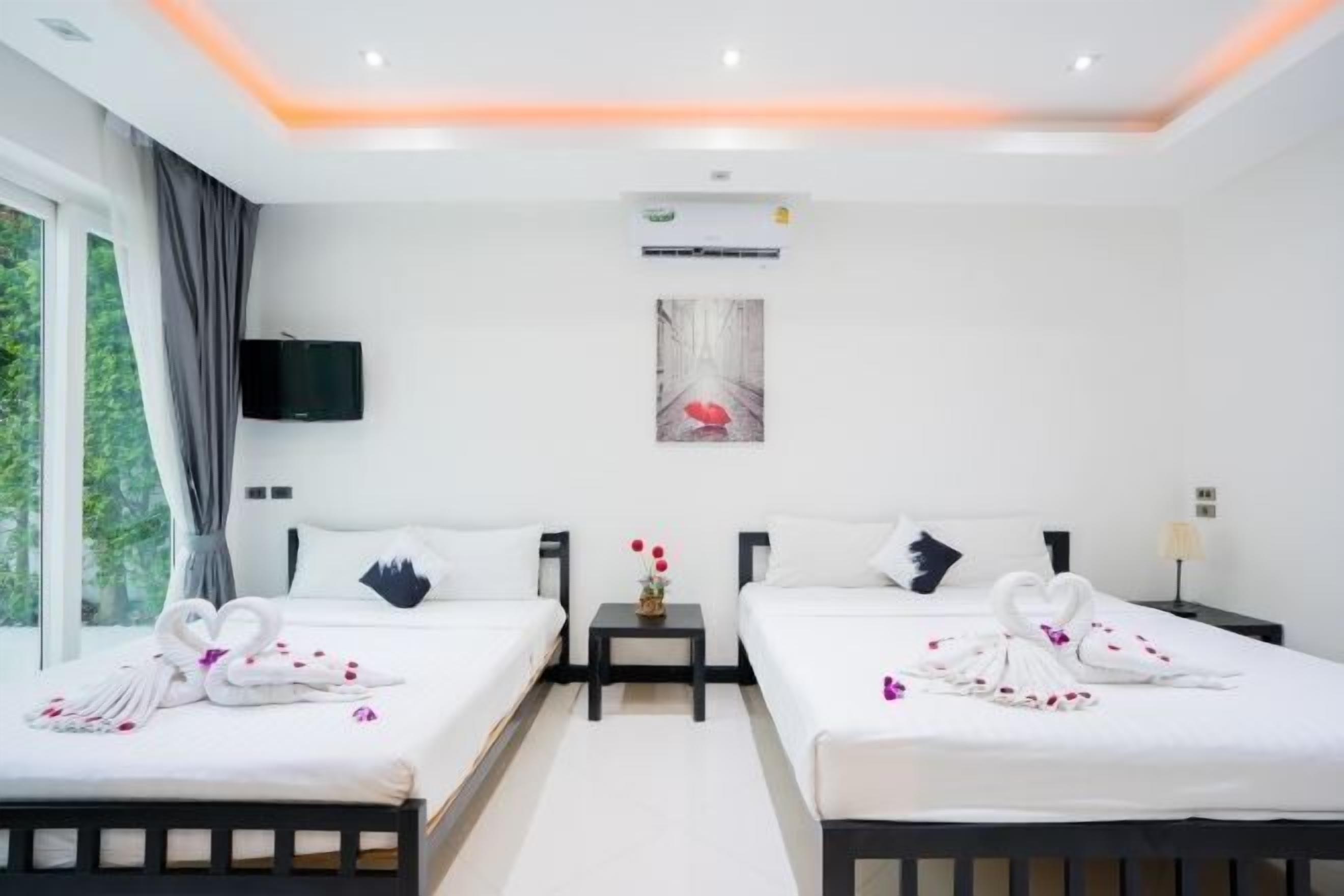 A hotel room with two beds, a flat-screen TV, a painting, and a small table with flowers.