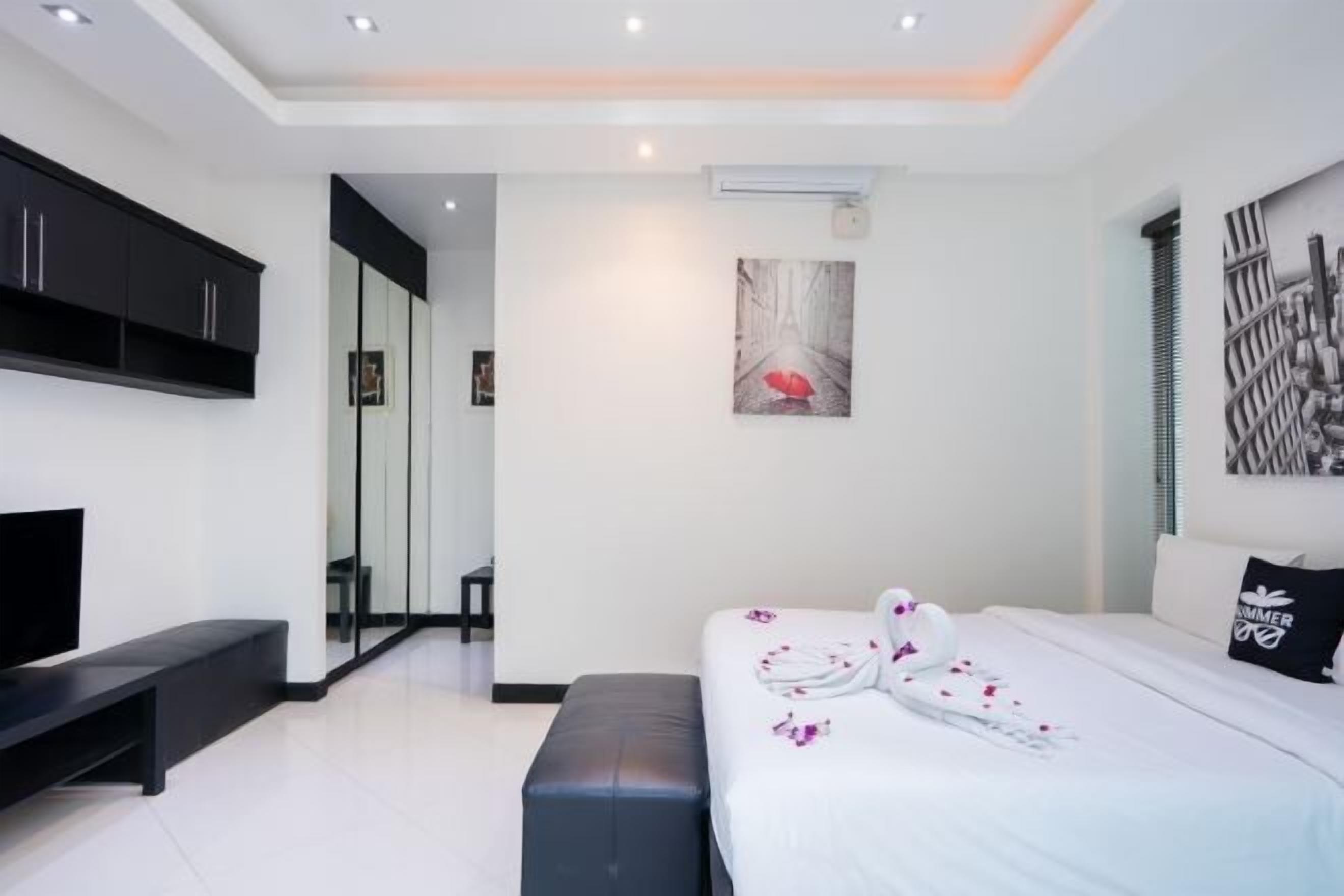 A modern bedroom with a large bed, a TV, a bench, and a painting on the wall.