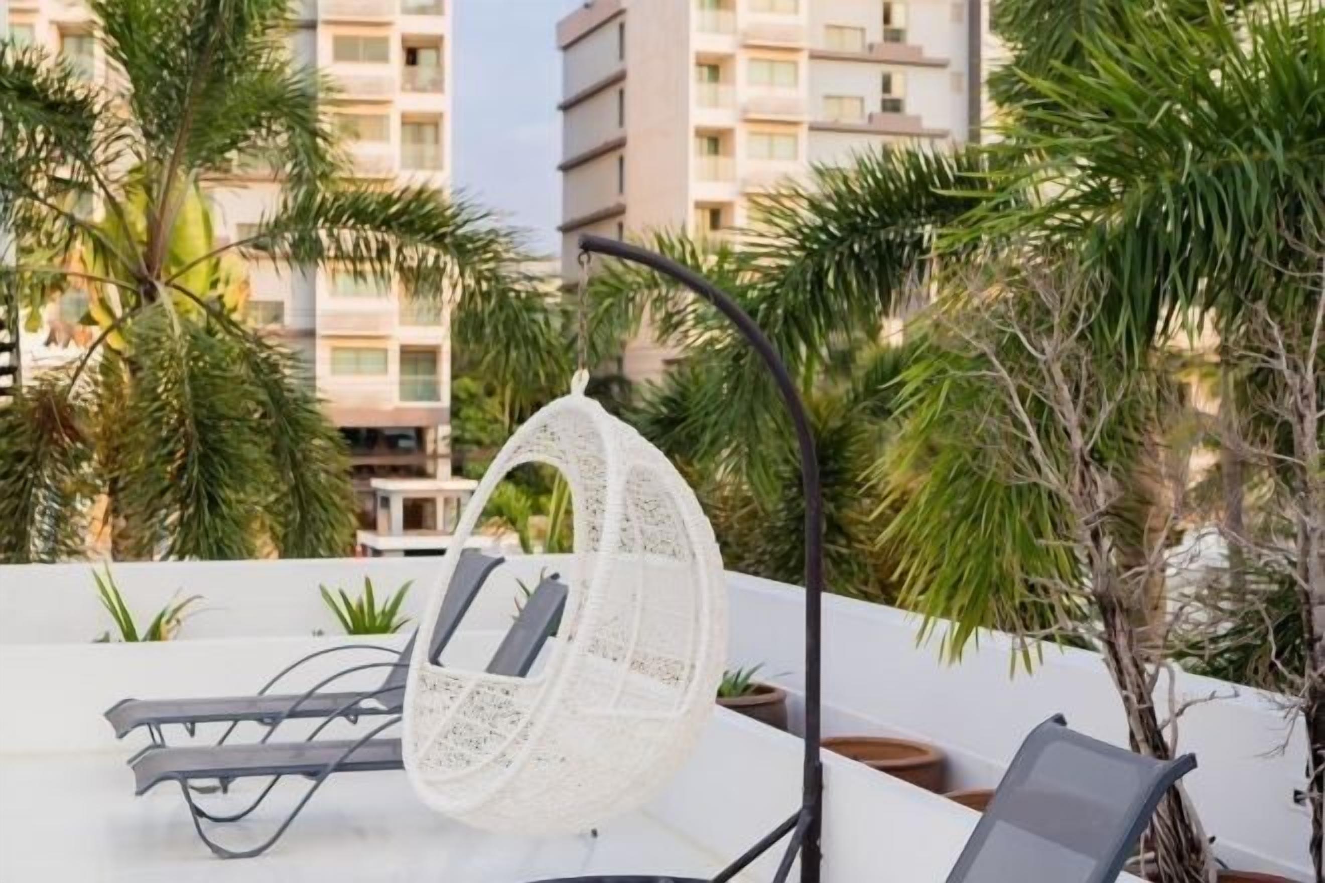 A rooftop terrace with a hanging chair, lounge chairs, and potted plants.