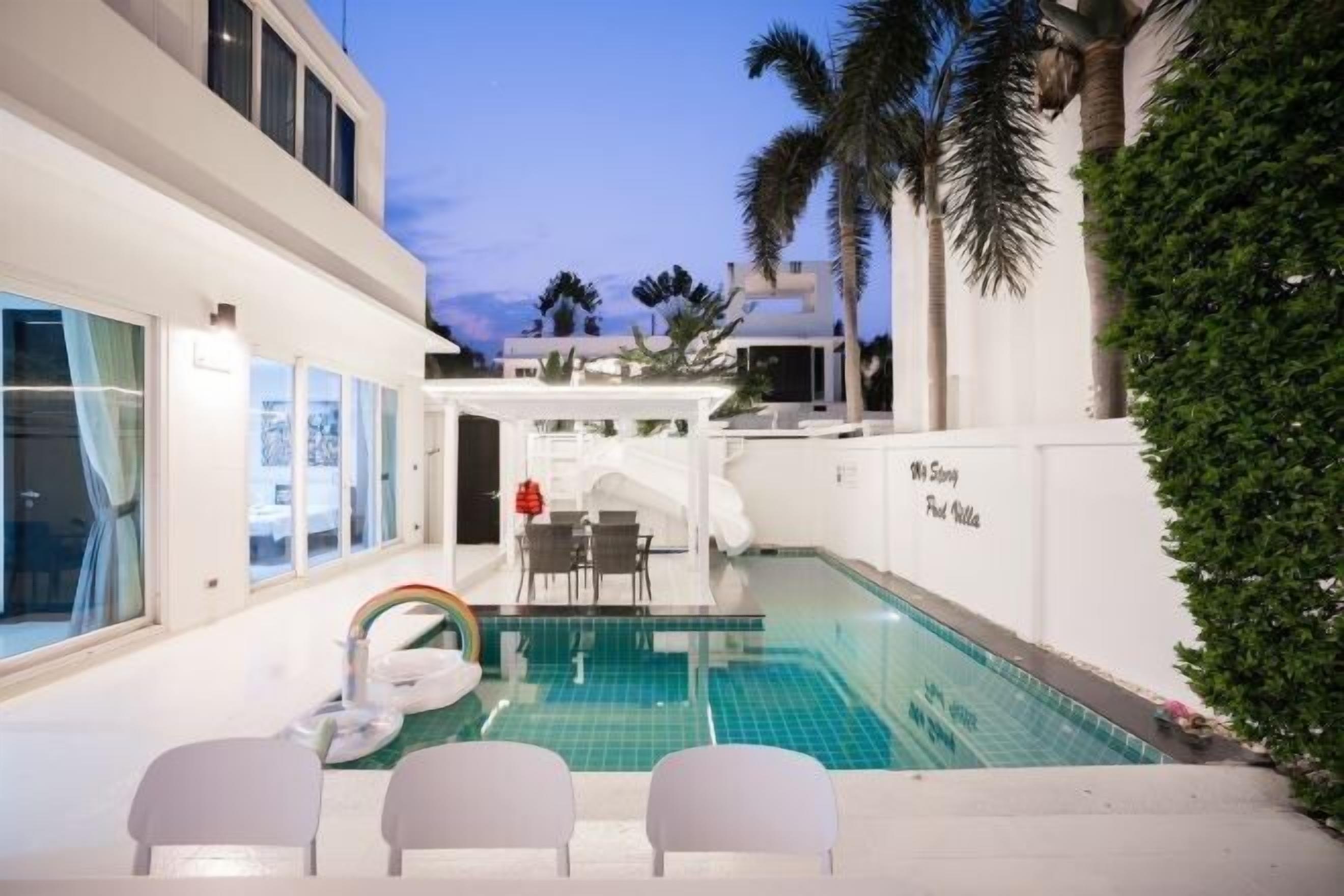 A modern pool area with a glass enclosure, white walls, and a small seating area with chairs.
