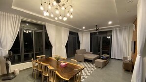 A modern living room with a wooden dining table, sofas, and a ceiling light fixture. - MyGarden Nam Phuong Lakeview (Bao Loc)