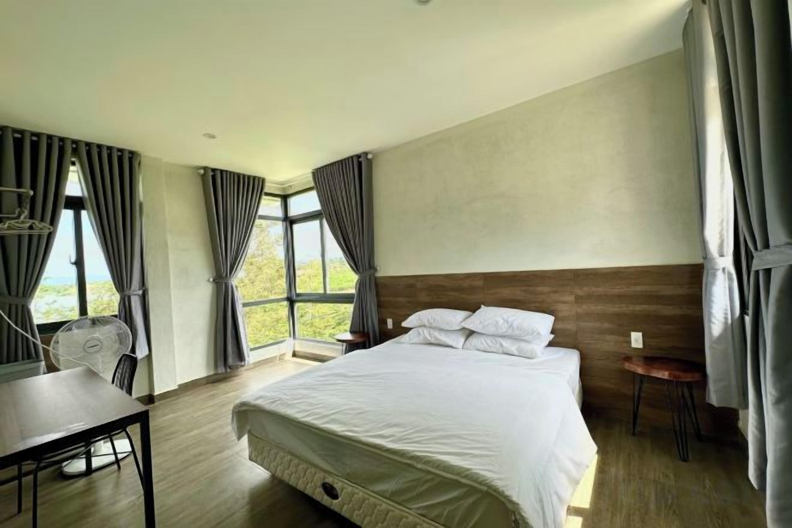 Habitación de hotel con una cama grande, un escritorio y una silla. Cuenta con ventanas con cortinas y vistas al exterior.