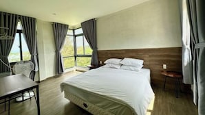 A modern hotel room with a large bed, a small table, and a fan. - MyGarden Nam Phuong Lakeview (Bao Loc)