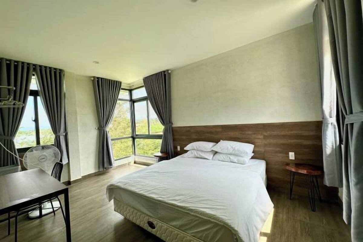 A modern hotel room with a large bed, a small table, and a fan.