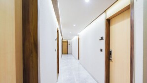 Un pasillo con paredes blancas, puertas de madera y suelo de mármol.