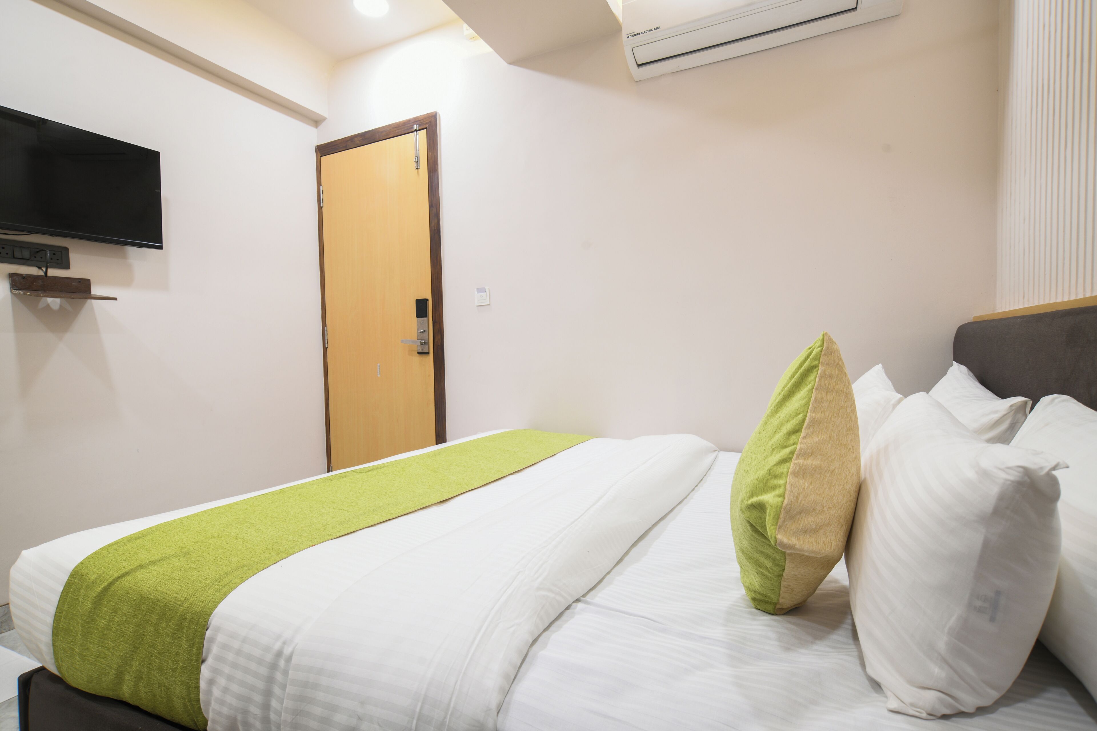 A hotel room with a bed, a television mounted on the wall, and an air conditioning unit.