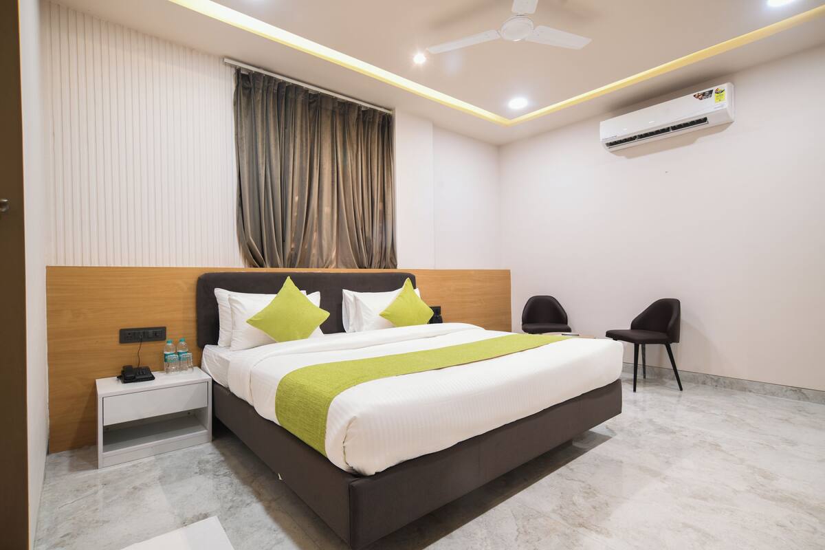 A modern hotel room with a large bed, bedside tables, a desk, a chair, and an air conditioning unit.