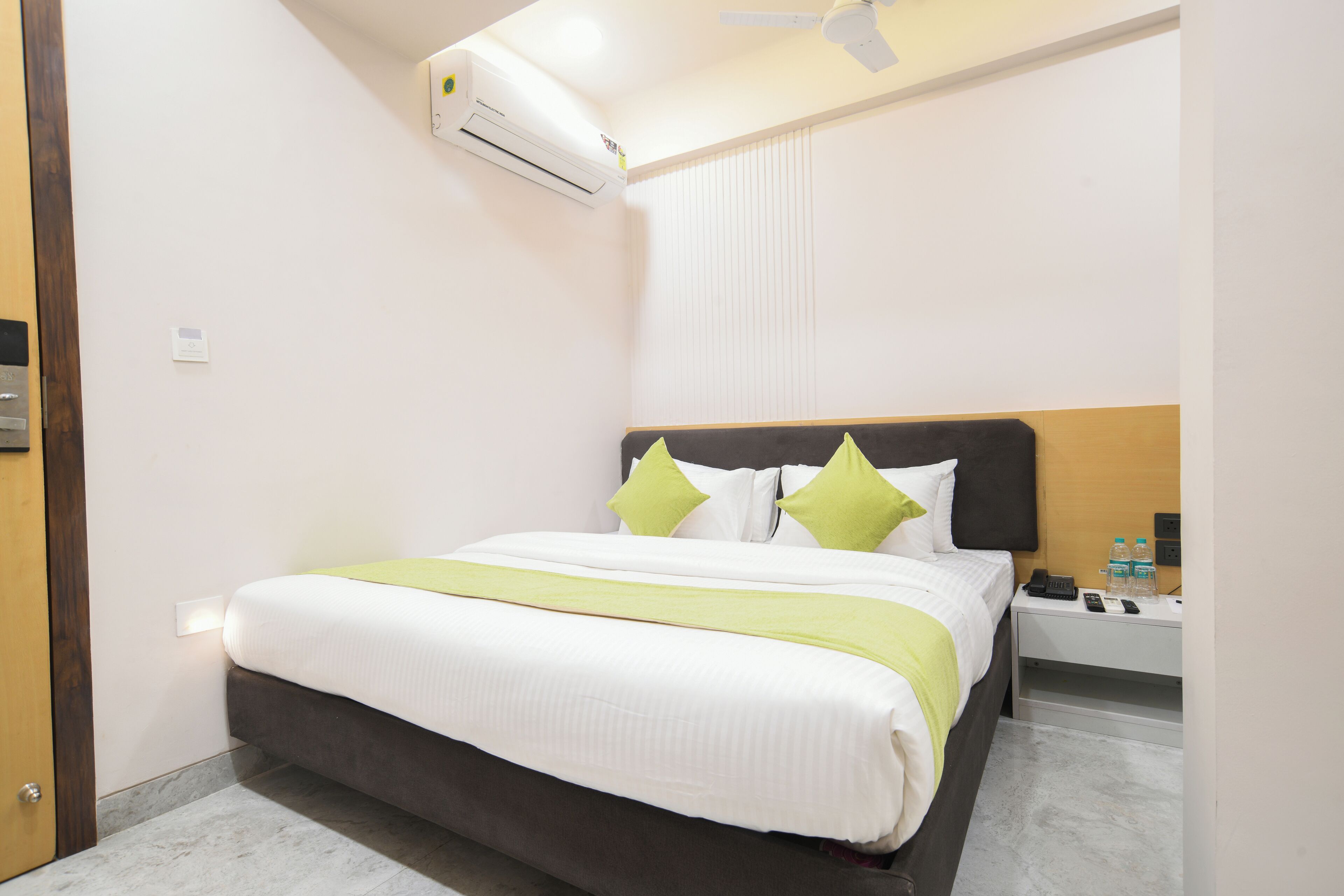 A hotel room with a bed, bedside table, and an air conditioning unit.