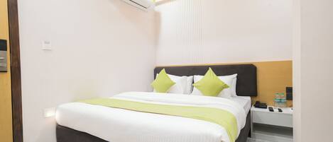 A hotel room with a bed, bedside table, and an air conditioning unit.