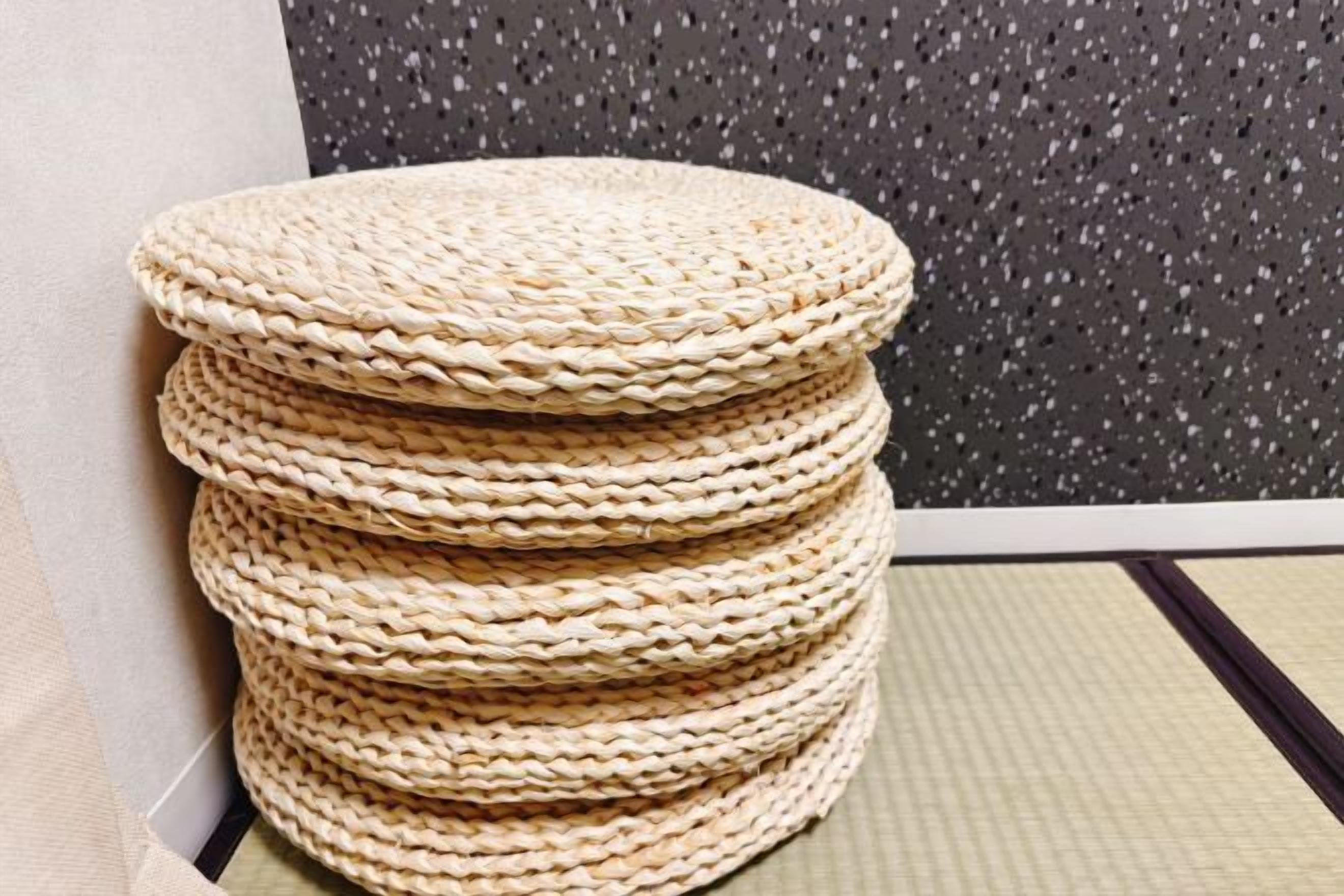 A stack of woven round mats in a room with a speckled wall and a tatami mat floor.