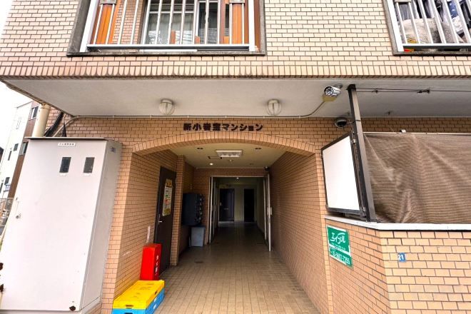 A building entrance with a sign above the door, a covered walkway, and a utility box to the left.