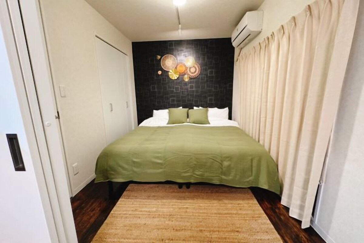 Ein Schlafzimmer mit Bett, Wand mit dunklem Muster, grüner Bettdecke und gewebtem Teppich.