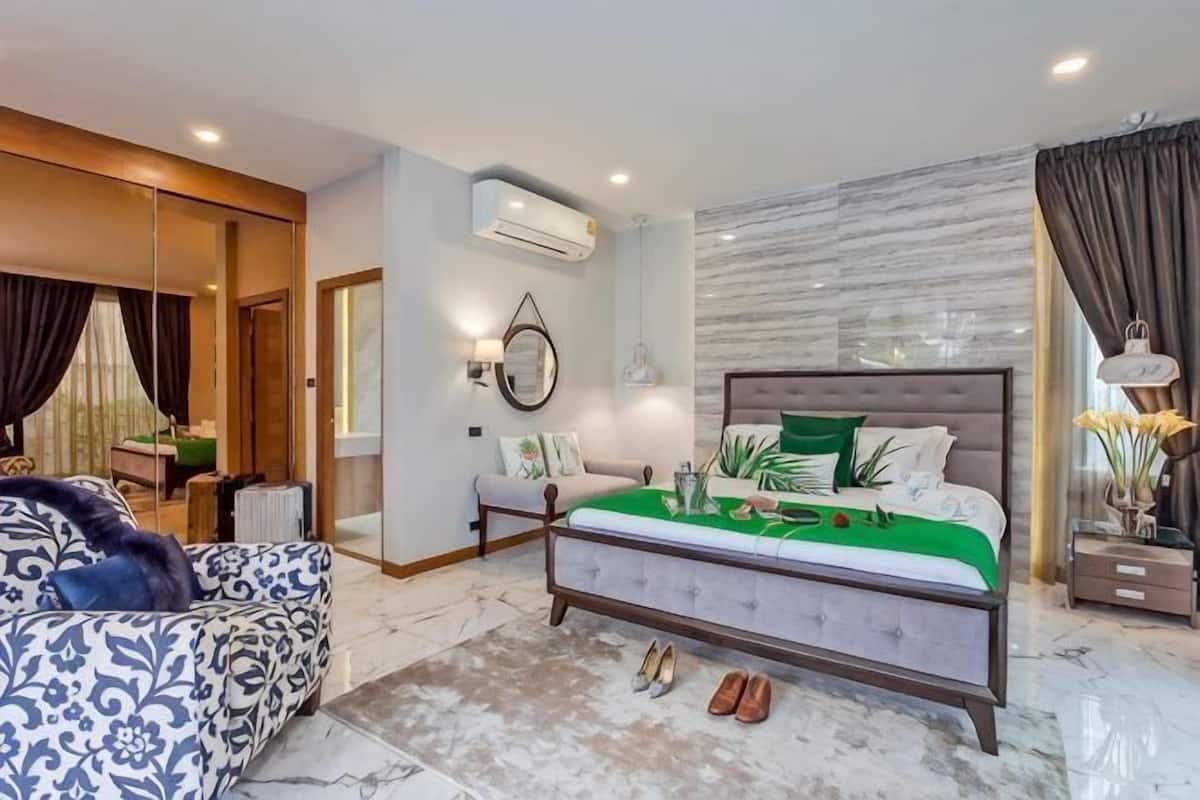 A modern bedroom with a large bed, a sofa, a mirror, and a wall-mounted air conditioner.
