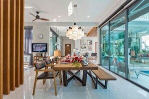 Un espace repas moderne avec une table en bois, des chaises et un banc. On y trouve également un téléviseur, une horloge et une fenêtre donnant sur l’extérieur.